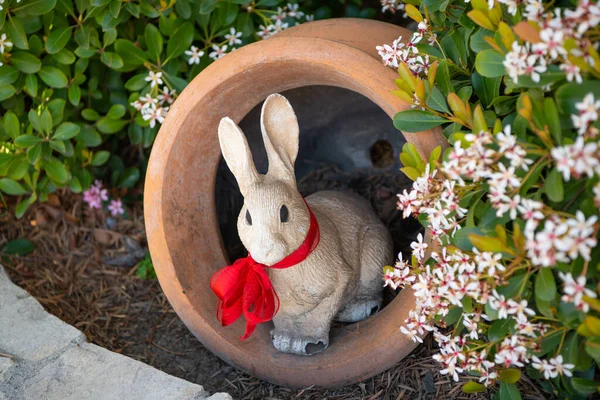 stock image Rabbit figurine in garden pot. Rabbit sculpture in garden. White rabbit statue with red bow. Garden rabbit bunny outdoor decor.