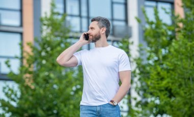 Yetişkin bir adamın dışarıda telefonu var. Sokakta telefonla konuşan bir adam var. Dışarıdaki adam aradı. Bir adamın telefon edip konuştuğu bir fotoğraf..