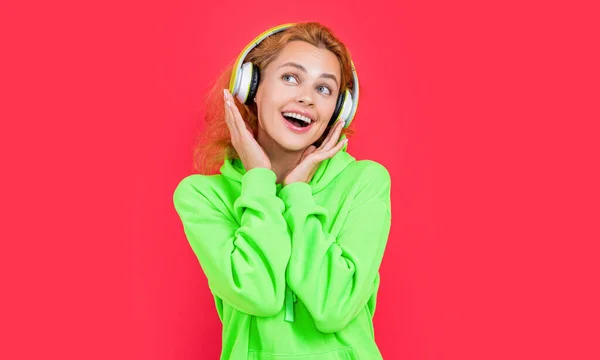 photo of cheerful cool woman listen music in headphones. redhead cool woman listen music on color background. cool woman listen music isolated on red background. cool woman listen music at studio.