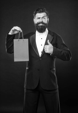 Smokinli, papyon takan, siyah arka planda, alışveriş çantalı mutlu bir adam. Alışveriş satışı. kopyalama alanı. başparmak yukarı.