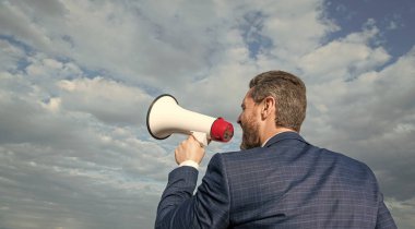 back view of businessman shout in loudspeaker on sky background. promotion.
