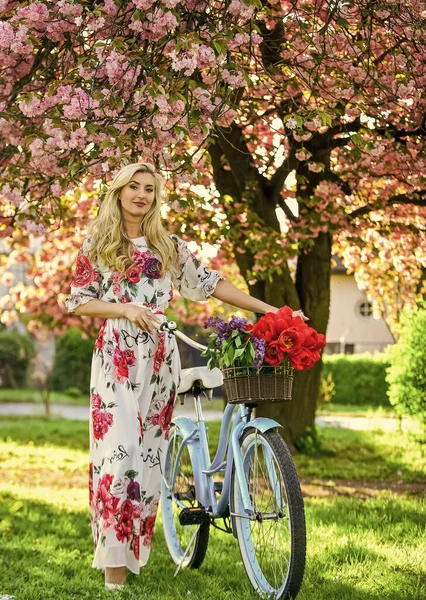 giyinmiş güzel bir kadın. Klasik bisikletli kız. Çiçekli sakura ağacı. Yaz modası ve güzellik. Bayan parkta yürüyor. Pembe kiraz ağacı çiçeği. Kız geçmişe dönük bisikletle çiçek taşıyor..