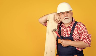 tired old man woodworker in helmet on yellow background.