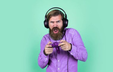 Olgun sakallı adamın uzun saçları var. Kulaklık takıyor. TV oyun konsolu kullanıyor..