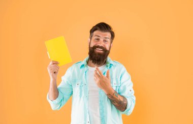 cheerful hipster guy point finger on notebook on yellow background, reader.