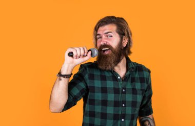 Seve seve söylerim. Erkek karaoke şarkıcısı. Olgun karizmatik erkek vokalist. Mikrofonda şarkı söyleyen sakallı adam. Sahnede özgüven ve karizma. Kareli gömlek giyen sakallı bir adam. rock müzik.