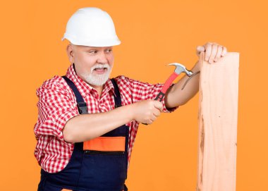 cheerful senior man woodworker in hard hat on yellow background.