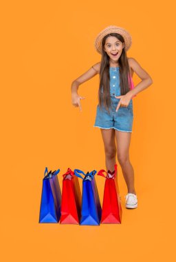 Mutlu genç kız sarı arka planda alışveriş torbalarını işaret ediyor. tam uzunluk.