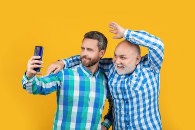 Mutlu kuşak erkeklerin telefonda selfie çektikleri bir fotoğraf. Nesiller boyu insanlar selfie 'yi sarıda izole ederler. Stüdyoda selfie çekiyorlar. Nesiller boyunca erkekler arka planda özçekim yaparlar..