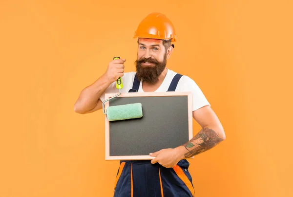 Positive Mann Renovierer Helm Und Arbeitskleidung Halten Farbroller Und Tafel — Stockfoto
