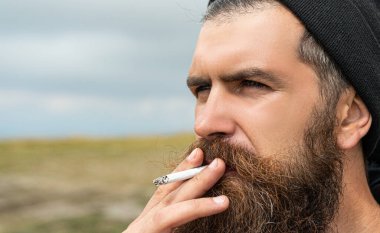 Sakallı adam, fotokopi odasıyla sigara içiyor. Dağda sigara içen bir adamın fotoğrafı. Dışarıda sigara içen bir adam. Sakallı adam sigara içiyor..