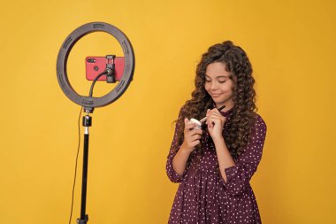 cheerful child blogger with long curly hair making video for blog hold powder brush.