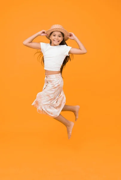 feel so free. barefoot kid feel freedom. full of happiness. summer kid fashion. little girl jumping high on yellow background. energetic kid on vacation. super active child jump in straw hat.