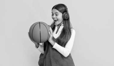 Okul çantalı ve sarı arka planda basketbol topu olan kulaklıklı çocuk şaşırdı..