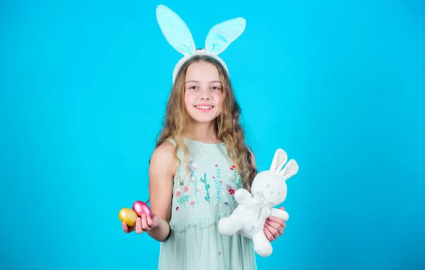 复活节快乐 快乐的小女孩戴着复活节兔子的耳朵 小女孩在兔子头带拿着彩蛋和玩具 可爱的女孩与可爱的填充兔子玩具 复活节兔子是复活节的象征 — 图库照片
