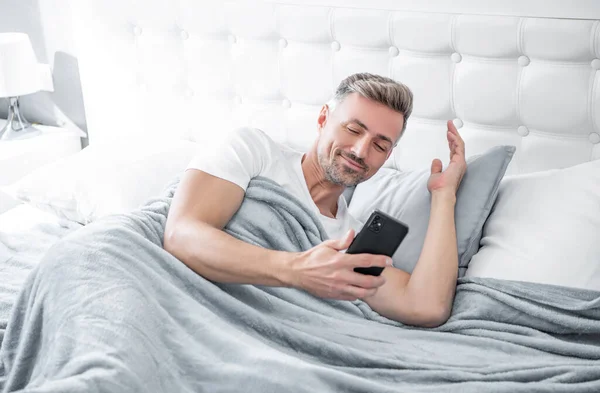 stock image happy mature man in bed chatting on phone.