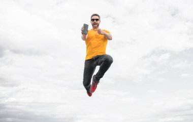 man jumping and presenting smartphone on sky background.