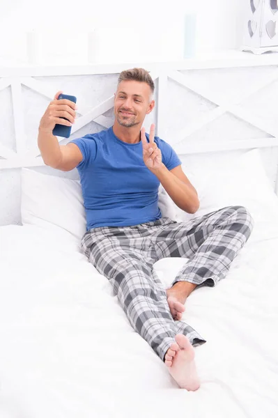 blogging man with phone wear pajama, gesturing. blogging man with phone in bed. photo of blogging man with phone at home. blogging man with phone in bedroom.