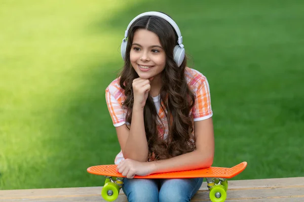 外でスケートボードをしてる10代の女の子 スケートボードを持つ10代の女の子の写真は音楽を聴く スケートボードのアウトドアを持つ10代の女の子 ヘッドフォンでスケートボードを持つ10代の女の子 — ストック写真
