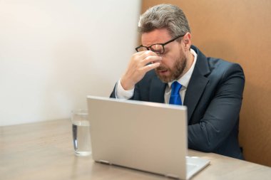 Çok çalışan yorgun iş adamının çalışırken başı ağrır. Çok çalışan iş adamının baş ağrısı var. Aşırı çalışan iş adamının fotoğrafı baş ağrısı yapar. Çok çalışan iş adamının başı ağrıyor..