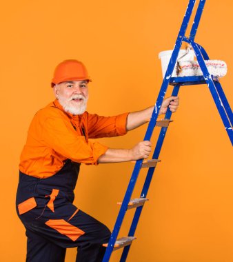 Boyacı merdiveni. Onarım yapmak için. İş elbiseli bir adam boş odaya duvar boyuyor. Boyalı kovayla şapkalı bir ressam. İnşaat işçisi boyama cephesi. termal yalıtım işe yarıyor.