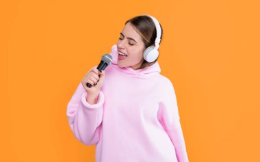 Sarı arka planda mikrofonu olan kulaklıklı genç bir kız..