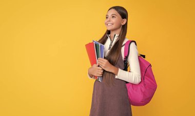 cheerful child with school backpack and workbook on yellow background.