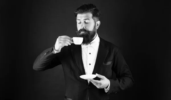 man in tuxedo bow tie with coffee cup. gentleman in formalwear smell coffee on black background.