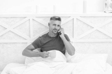 Sabah çayı ya da yatakta kahve içerken cep telefonuyla konuşan mutlu adam, ara..