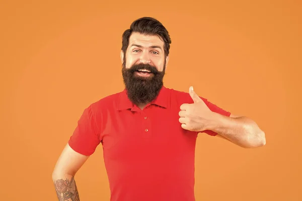 一个留着胡子的快乐男人 他的T恤上有胡子 他的大拇指长在橙色背景上 发型也很好看 — 图库照片