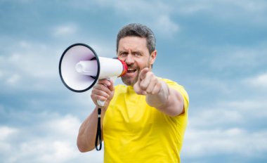 Sarı gömlekli adam arka planda hoparlörle bağır. işaret parmağı.