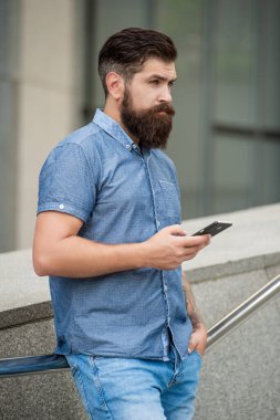 Dışarıda cep telefonu kullanan sakallı adam. Ciddi bir adam cep telefonu mesajlaşması, mobil iletişim için cihaz kullanıyor. Mobil teknoloji.
