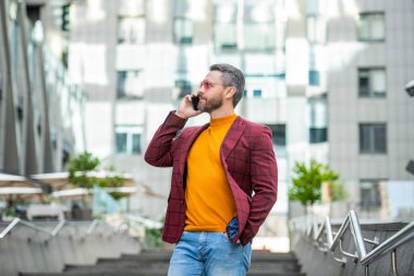 Dışarıdaki cep telefonundan arayan bir adam. Cep telefonundan arayan bir adamın görüntüsü. Adamın dışarıda cep telefonu görüşmesi var. Sokakta cep telefonu arayan bir adam var..