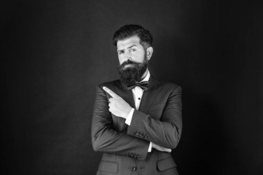Smokin papyonlu ciddi bir adam. Siyah arka planda resmi kıyafetli bir adam işaret ediyor. Erkek resmi moda. Boşluğu kopyala.