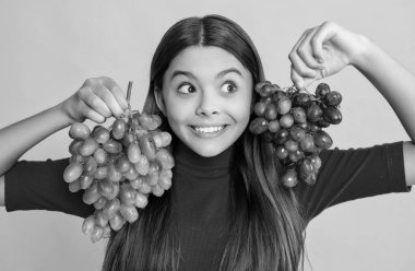 Şaşırmış genç kız sarı arka planda üzüm tutuyor..