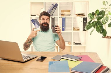 Ofis masasında oturmuş, kahve fincanını işaret eden mutlu iş adamı..