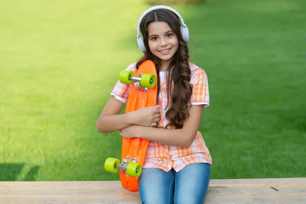 スケートボードの屋外で喜んで10代の女の子 ヘッドフォンでスケートボードを持つ10代の女の子 スケートボードを持ってる10代の女の子 スケートボードで10代の女の子の写真は音楽を聞く — ストック写真