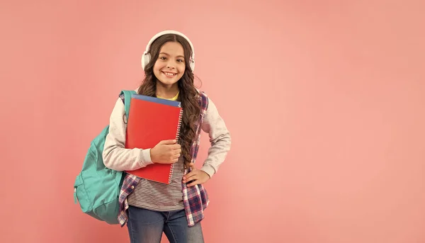 幸せなティーン女の子とともにバックパックとワークブックを身に着けていますヘッドフォンでピンクの背景にコピースペース 現代生活 — ストック写真