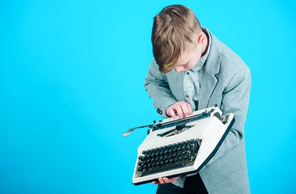 Using a typing machine. Small kid typewriting on old typewriter. Smart schoolboy with vintage typewriter. Cute boy with typewriter. Little boy holding retro typewriter on blue background, copy space.