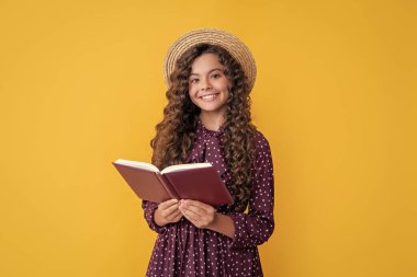 cheerful child with frizz hair read book on yellow background.