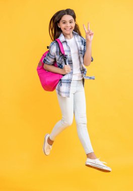 Zıplayan liseli kız sarıda izole edilmiş. Stüdyodaki genç kız. Arkaplanda genç bir kız var. Sırt çantalı liseli kızın fotoğrafı.