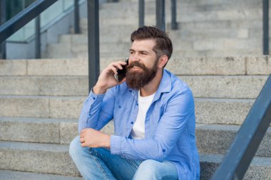 Gülümseyen adamın sokakta akıllı telefonu var. Adamın fotoğrafında akıllı telefon var. Adamın dışarıda akıllı telefonları var. Adamın dışarıda akıllı telefonu var..