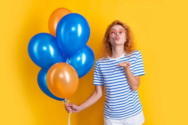 woman blow kiss with birthday balloon in sunglasses. happy birthday woman hold party balloons in studio. woman with balloon for birthday party isolated on yellow background.