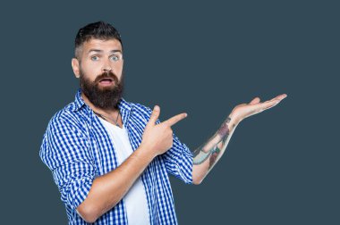 Şaşırmış bir adam gri arkaplanda sunum yapan kareli gömlek giyer..