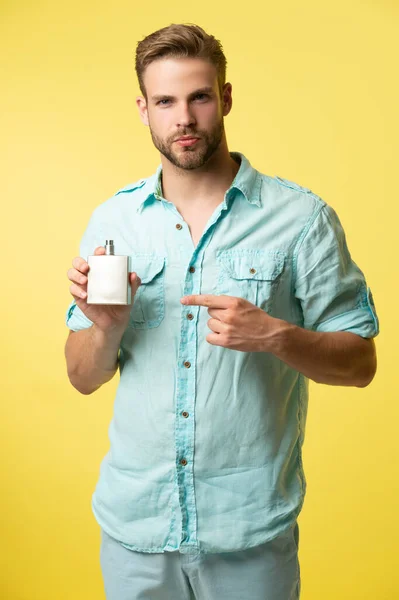 photo of man point finger on perfume. man hold perfume. man hold perfume isolated on yellow. man hold perfume in studio background.