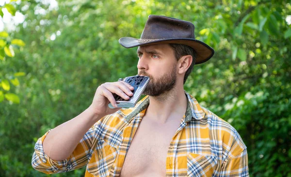 photo of western man drinking whiskey flask. western man with whiskey flask. western man with whiskey flask outdoor. western man with whiskey flask wear checkered shirt.