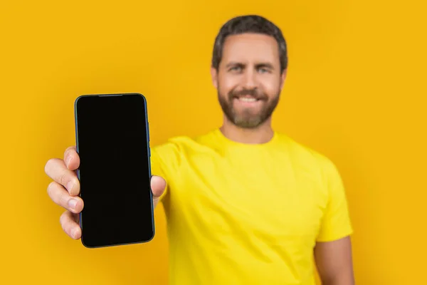 stock image selective focus of man showing smartphone app on background. man showing smartphone app in studio. photo of man showing smartphone app. man showing smartphone app isolated on yellow.