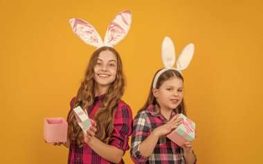 Tavşan kulaklı neşeli Paskalya çocukları sarı arka planda hediye kutusunu tutarlar..