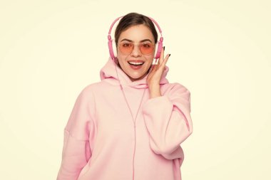 Happy young woman in pink hoodie and glasses listening to music in headphones isolated on white.