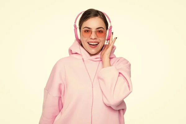 stock image Happy young woman in pink hoodie and glasses listening to music in headphones isolated on white.